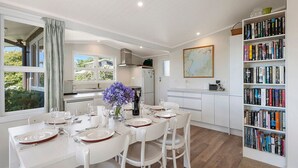 A modern kitchen with white cabinetry, a dining table set for four, and a bookshelf filled with books.