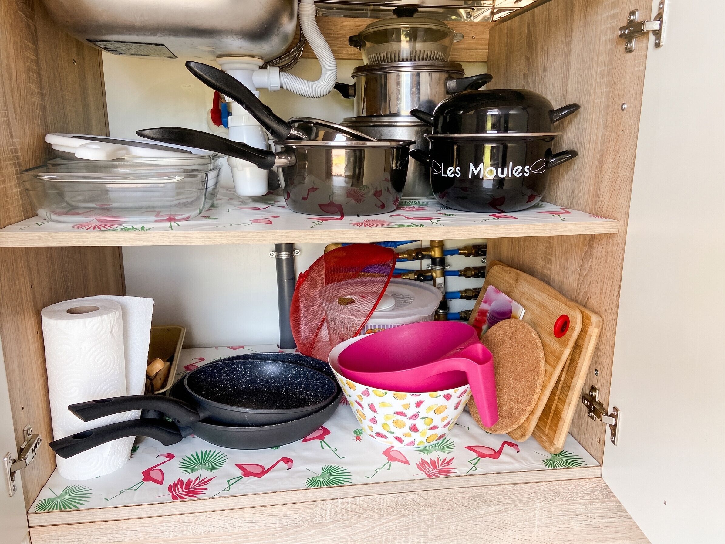 Un meuble de cuisine contenant des casseroles, des poêles et une planche à découper.