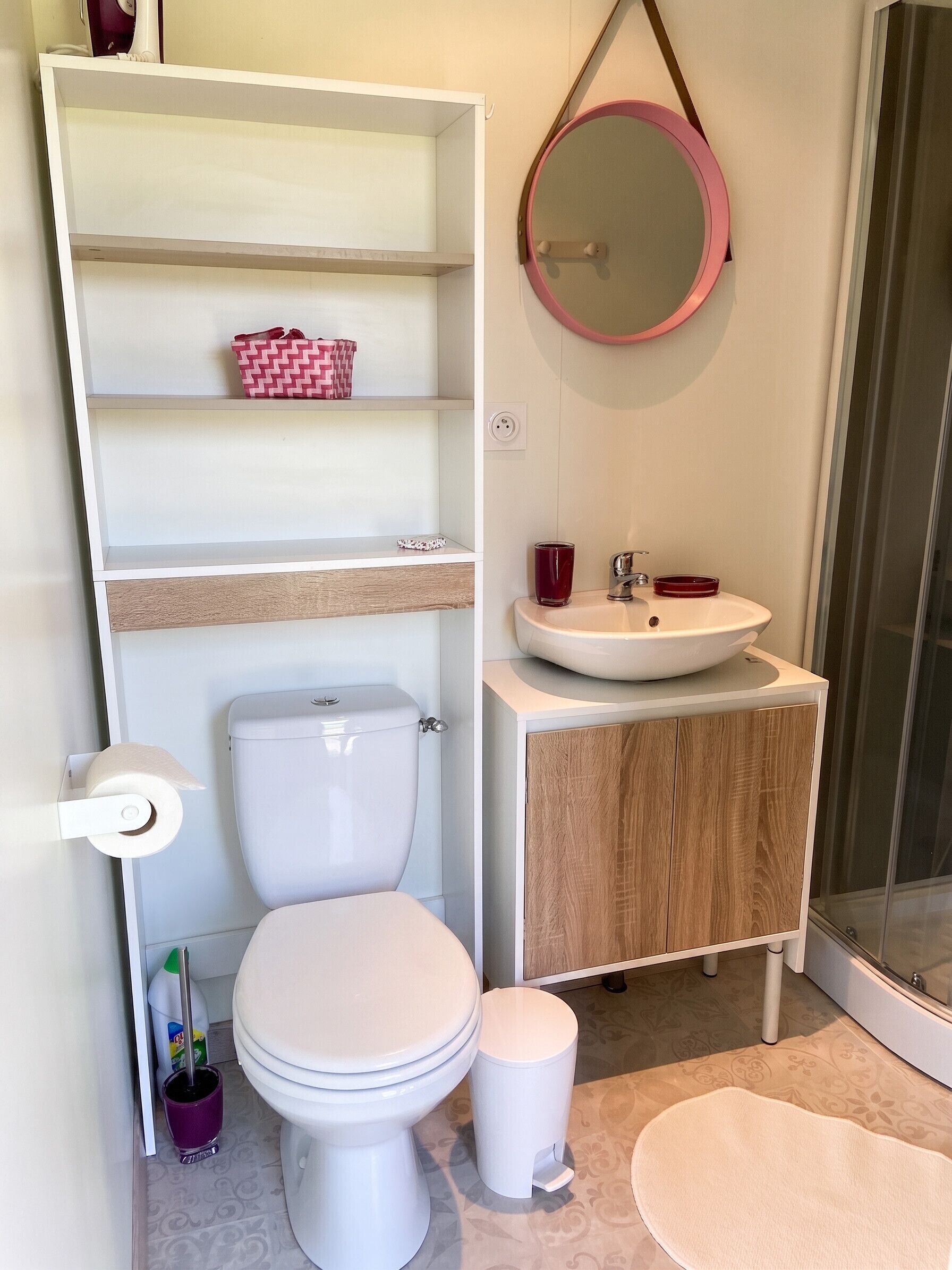 Un baño con inodoro, lavamanos, espejo, estantes y zona de ducha.