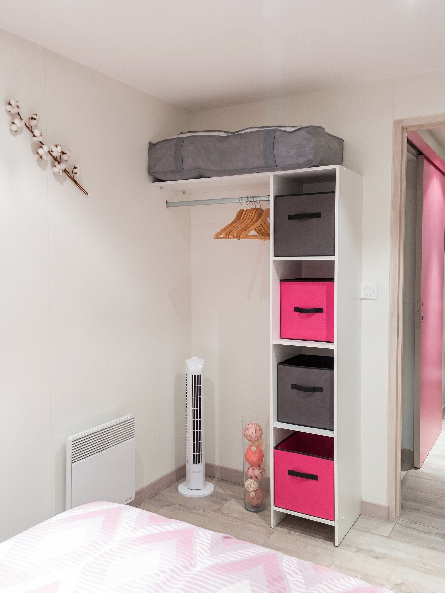 A bedroom with a bed, a wardrobe with drawers, a radiator, a heater, and a closet with a pink door.
