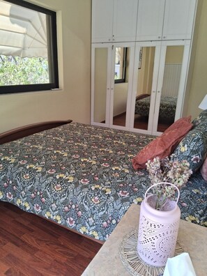 A bedroom with a bed, a window, a mirror, and a bedside table with a vase. - 3BR Greek Riviera Escape | Near Voula Beach & Athens Riviera (Voula)