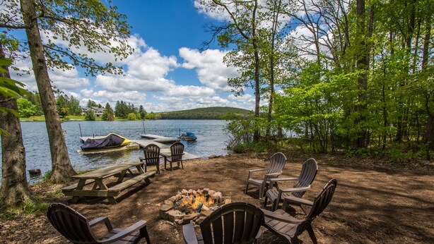 Un camping junto al lago con fogón, mesa de picnic y sillas Adirondack.