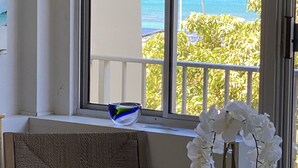 Ett rum med utsikt över havet, en stol, ett bord och en vas med vita blommor.