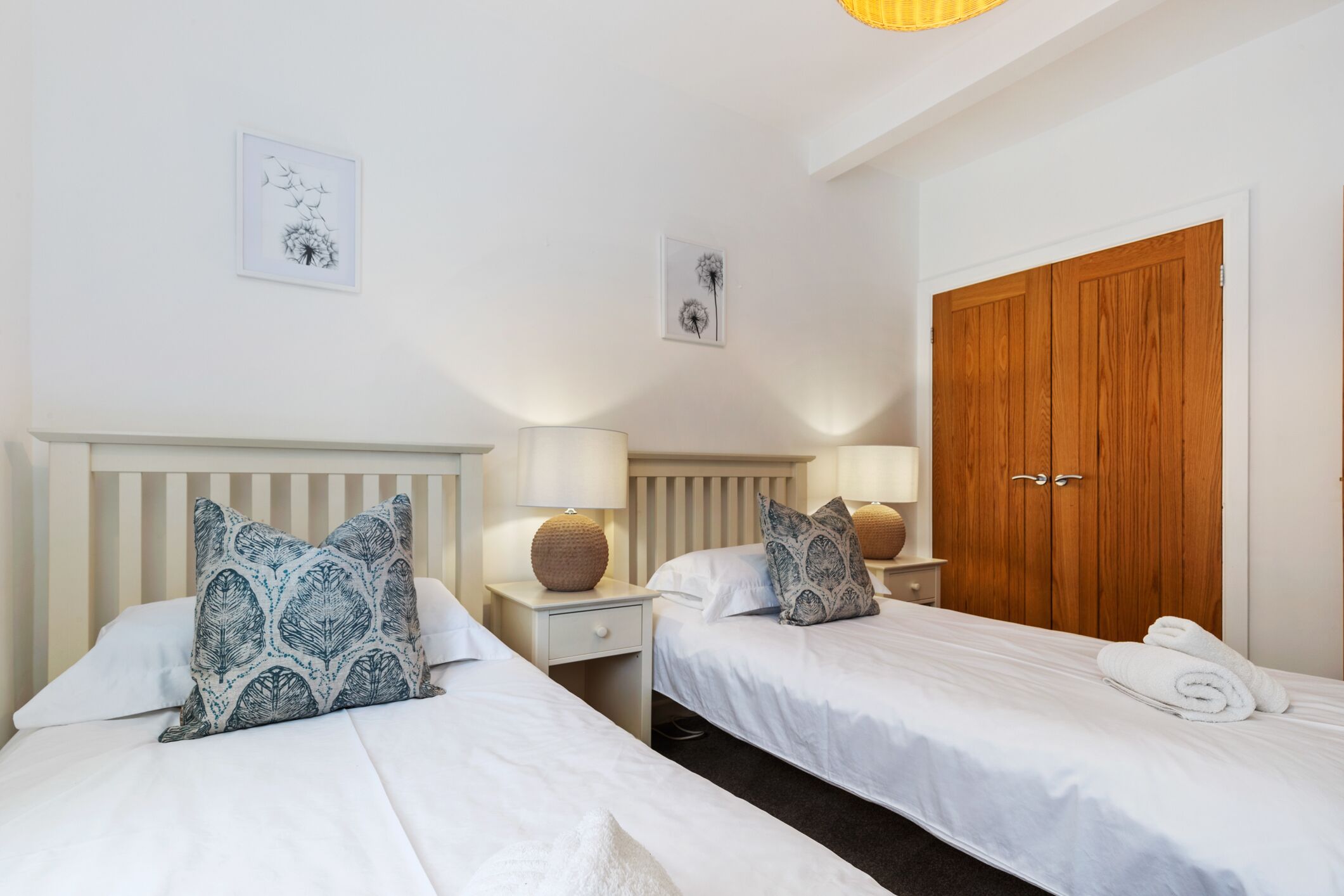 A hotel room with two beds, a wooden wardrobe, and a nightstand with a lamp.