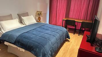 Un dormitorio con una cama, un escritorio, una silla, una lámpara y un televisor.