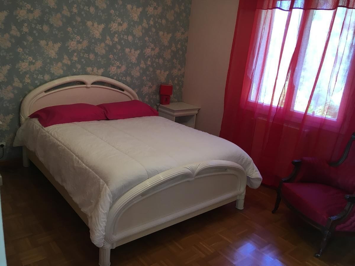 A bedroom with a bed, a nightstand, a chair, and a window with curtains.