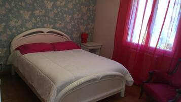 A bedroom with a bed, a nightstand, a chair, and a window with curtains.