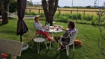 Two people seated at an outdoor table with a picnic setup, surrounded by greenery and trees.