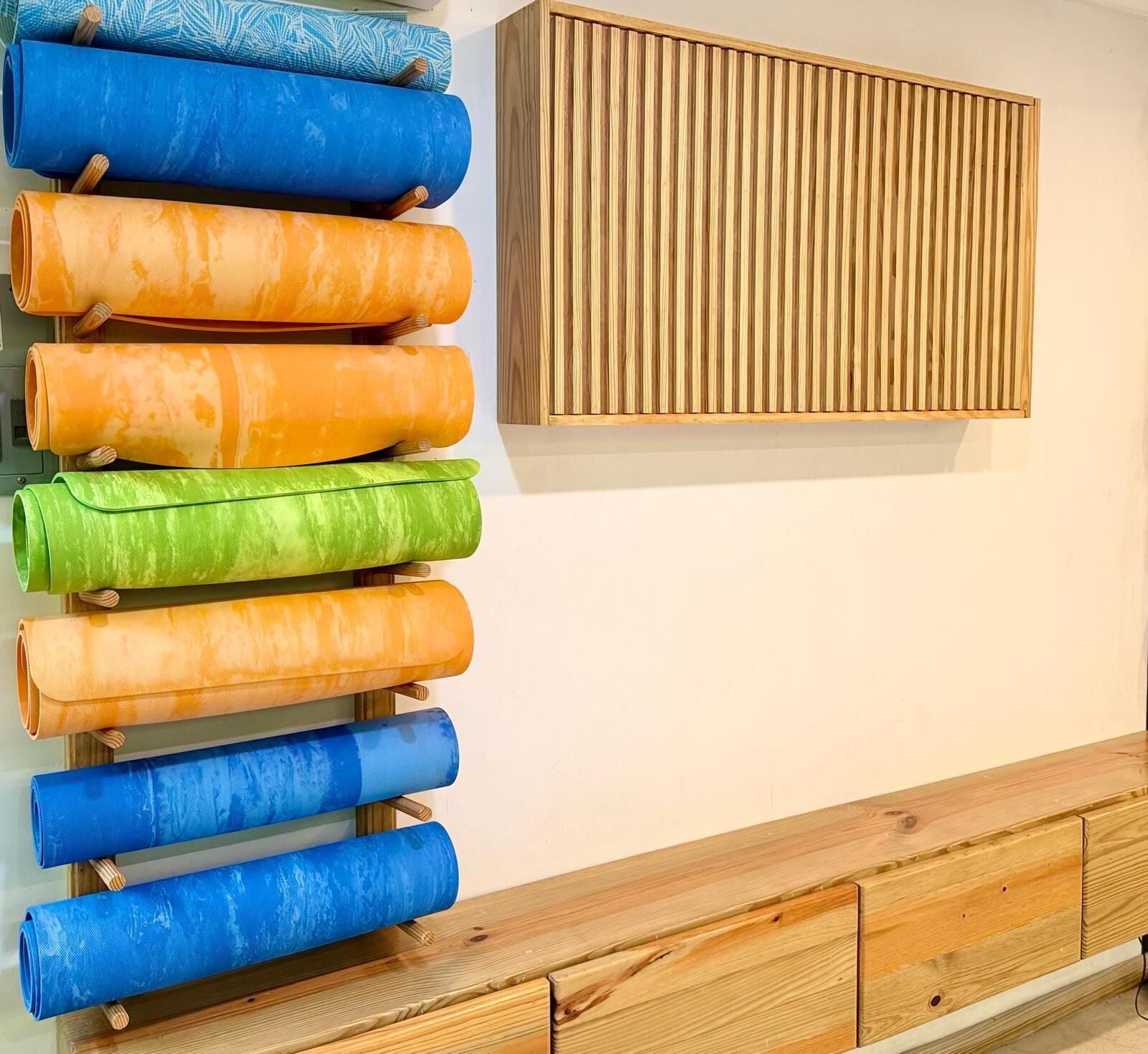 Un panel de listones de madera montado en la pared y un banco de madera con cajones.
