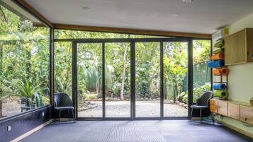 A spacious room with large sliding glass doors, a black cushioned seating area, and a wall-mounted shelf with rolled-up mats.