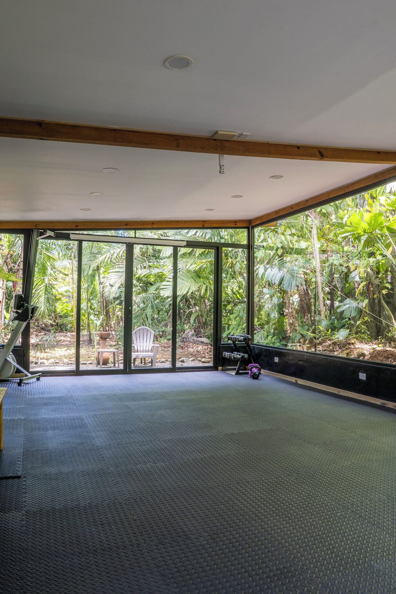 A spacious room with large windows, a ceiling fan, and exercise equipment.
