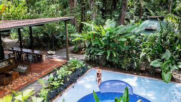 Una piscina rodeada de vegetación exuberante, con un área de estar cubierta y vistas al bosque.