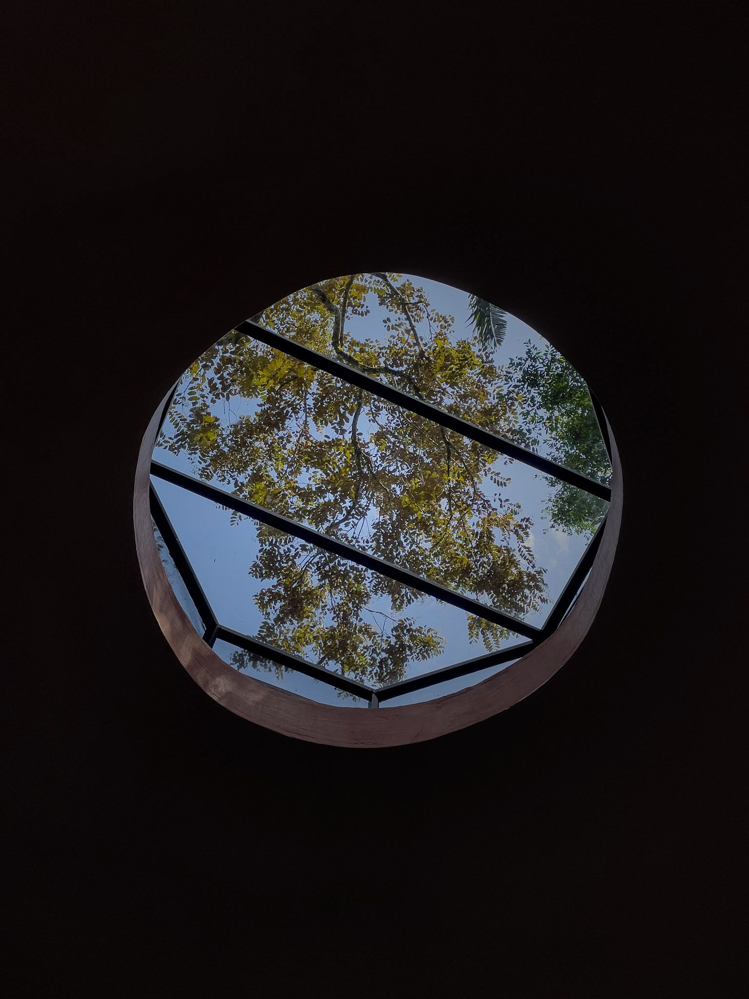 Una ventana circular con vistas a árboles y al cielo.