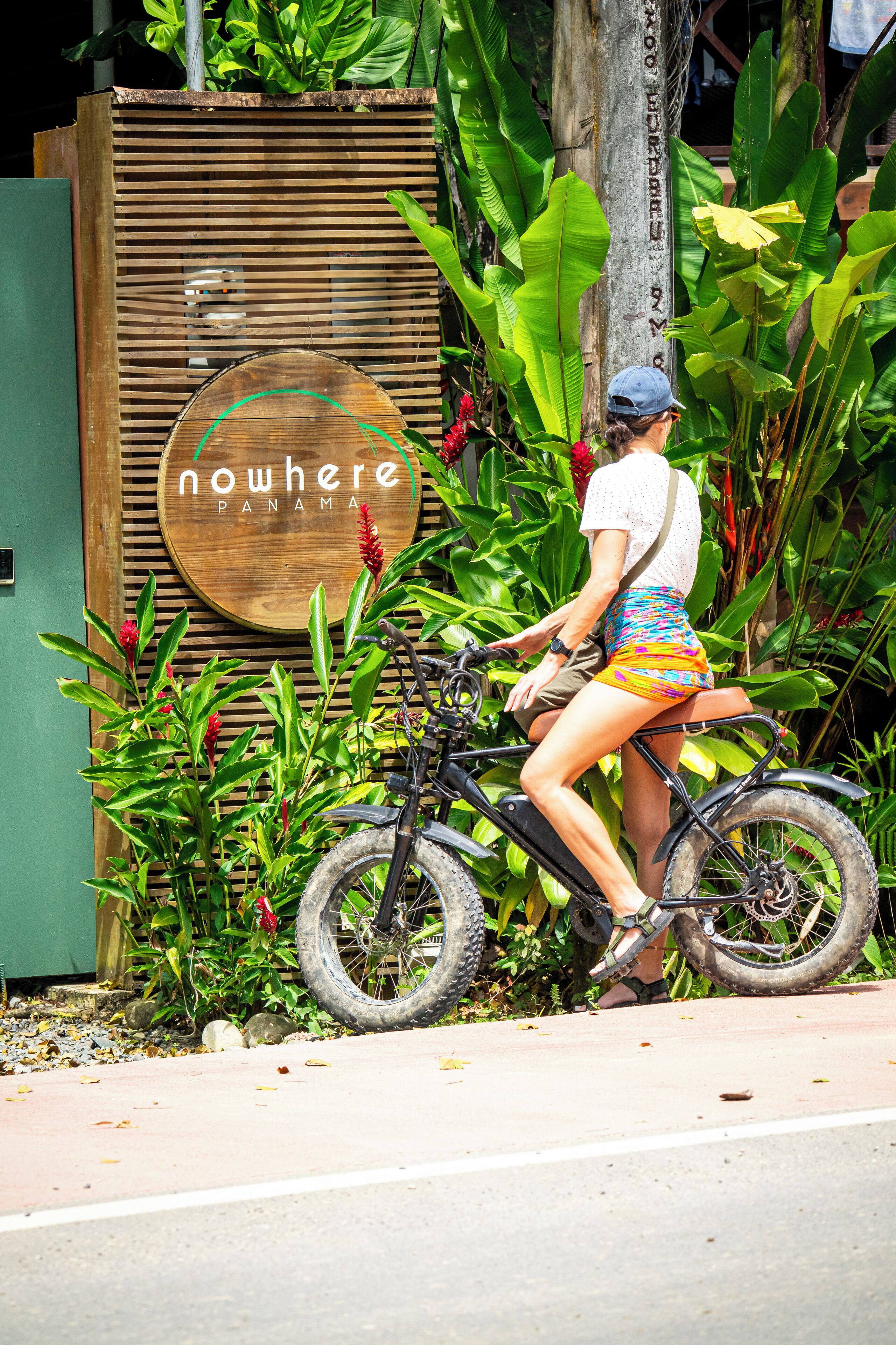A person riding a bicycle in front of a wooden sign with "nowhere Panama" written on it.