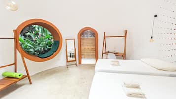 Habitación minimalista con una cama, un ventanal circular con plantas, una mesita y una silla.