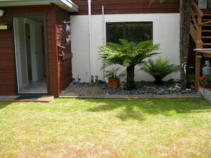 A residential property with a wooden exterior, a small garden with a palm tree, and a visible door. - Cooks Beach Gem - Cooks Beach Holiday Home (Cooks Beach)