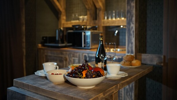 A breakfast setting with a bowl of fruit, a bottle of champagne, and a cup of coffee on a wooden table. - Mycologne (Cologne)