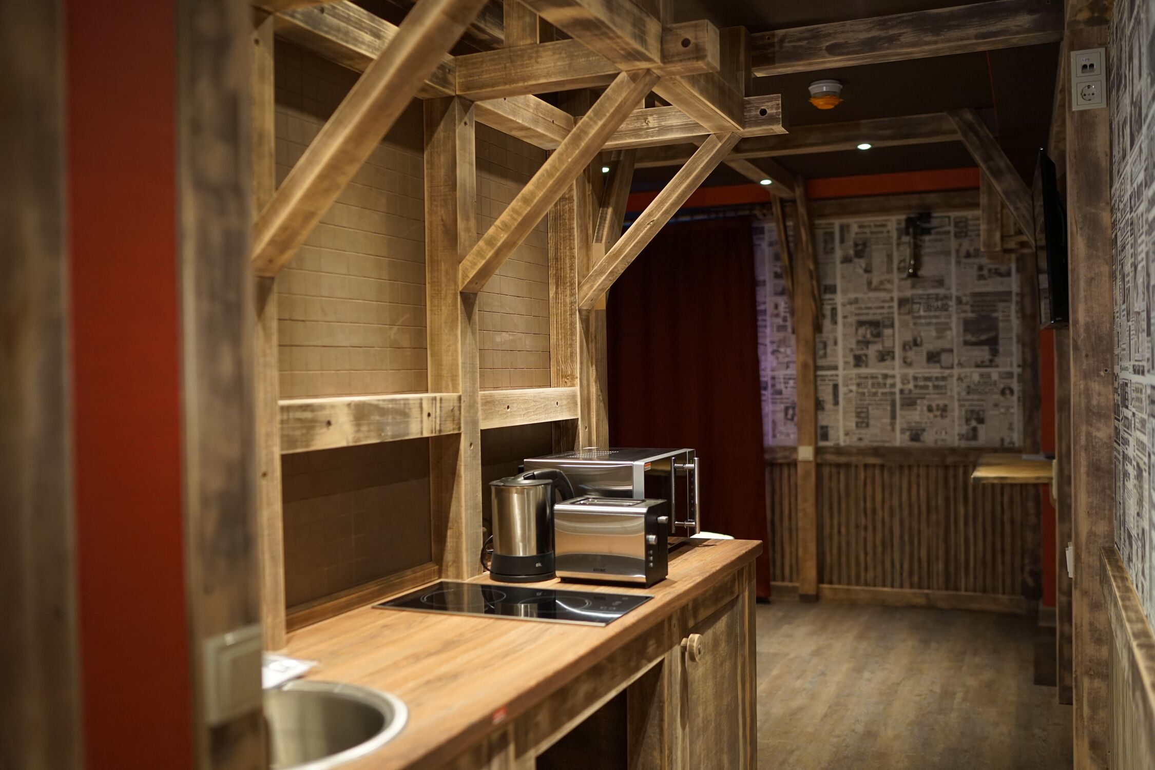 A narrow kitchen with wooden beams, a stainless steel kettle, and a toaster on a wooden countertop.