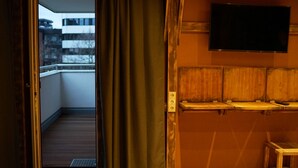 A room with a wooden floor, a sliding door leading to a balcony, a mounted television, and a small wooden table. - Mycologne (Cologne)