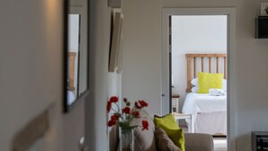 A bedroom with a wooden headboard, a bed with white bedding and a yellow pillow, a bedside table with a vase of red flowers, and a chair. - The Dairy - Luxury Cottage with Hot Tub and Views (Ludchurch)