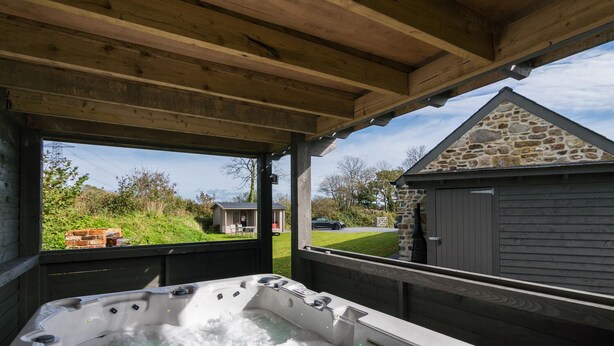 A hot tub under a wooden pergola with a stone building and a car in the background. - The Dairy - Luxury Cottage with Hot Tub and Views (Ludchurch)