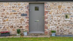 A stone building with a grey door, a sign reading "The Dairy," and two potted plants on the ground. - The Dairy - Luxury Cottage with Hot Tub and Views (Ludchurch)