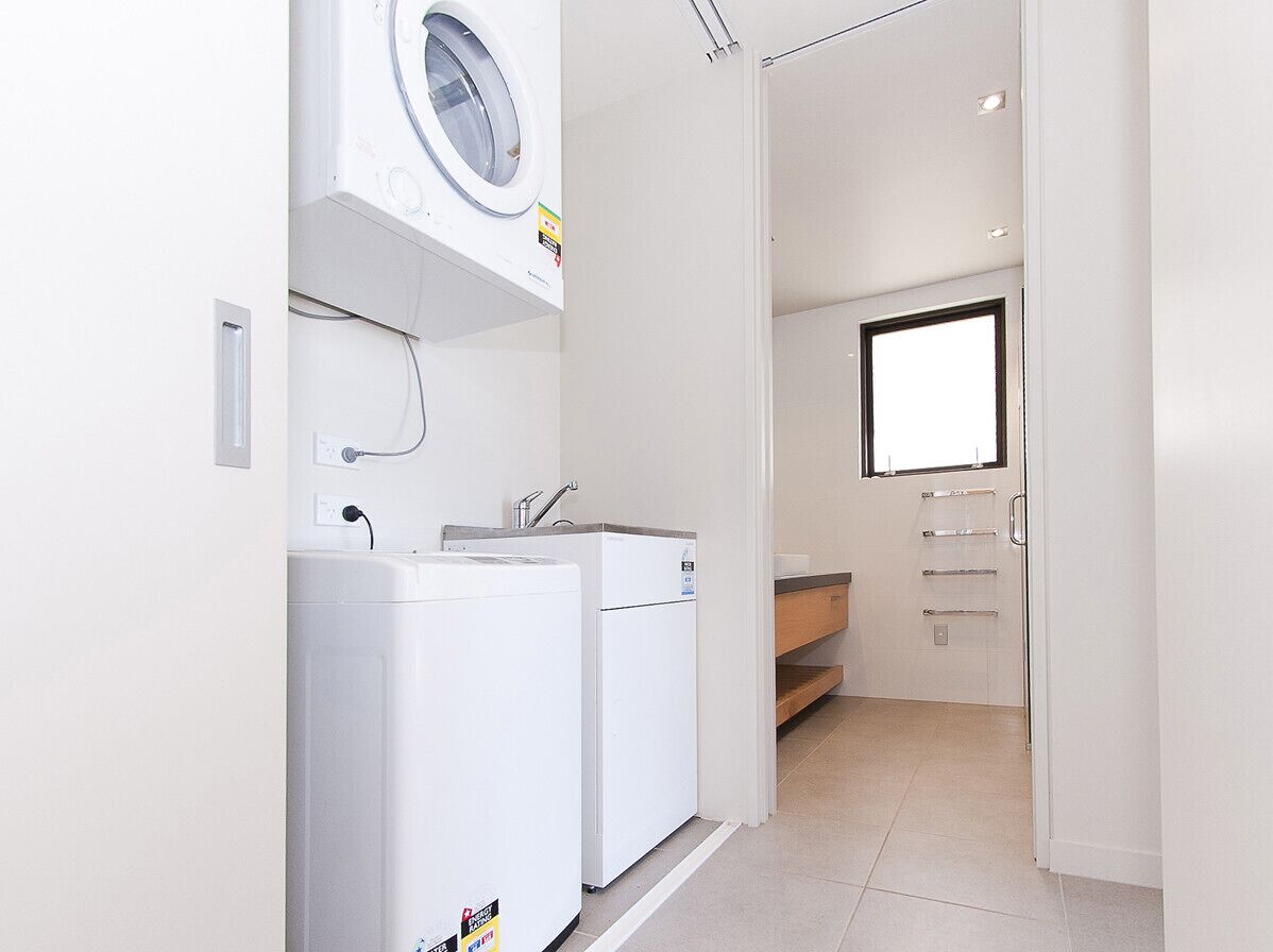 Une petite buanderie comprenant un lave-linge, un sèche-linge et un petit évier.