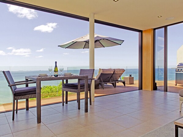 Un balcon avec une table, des chaises et un parasol, d’où l’on a vue sur la mer.