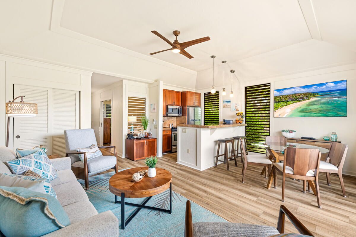A spacious living area with a sofa, coffee table, and dining set. A kitchen with wooden cabinets and a bar area is visible.