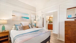 A bedroom with a large bed, a nightstand, a dresser, and a painting of a beach scene. - KIAHUNA BEACH HOUSE #50 NEW REMODEL GROUND FLOOR NEW AC TWIN BRIDGES GARDEN VIEW (Koloa)