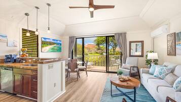 A spacious living area with a kitchen, dining table, and a large sliding glass door leading to a balcony.