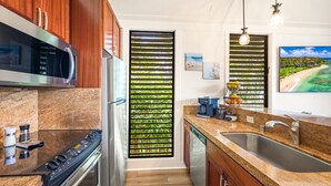 A modern kitchen with a stainless steel refrigerator, a built-in oven, and a granite countertop. - KIAHUNA BEACH HOUSE #50 NEW REMODEL GROUND FLOOR NEW AC TWIN BRIDGES GARDEN VIEW (Koloa)