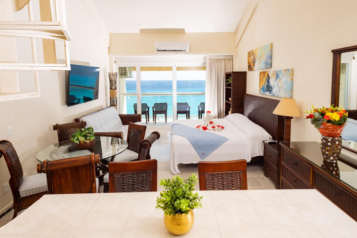 Ein Hotelzimmer mit Bett, Esstisch mit Stühlen, Fernseher, Balkon mit Meerblick und Blumenvase.