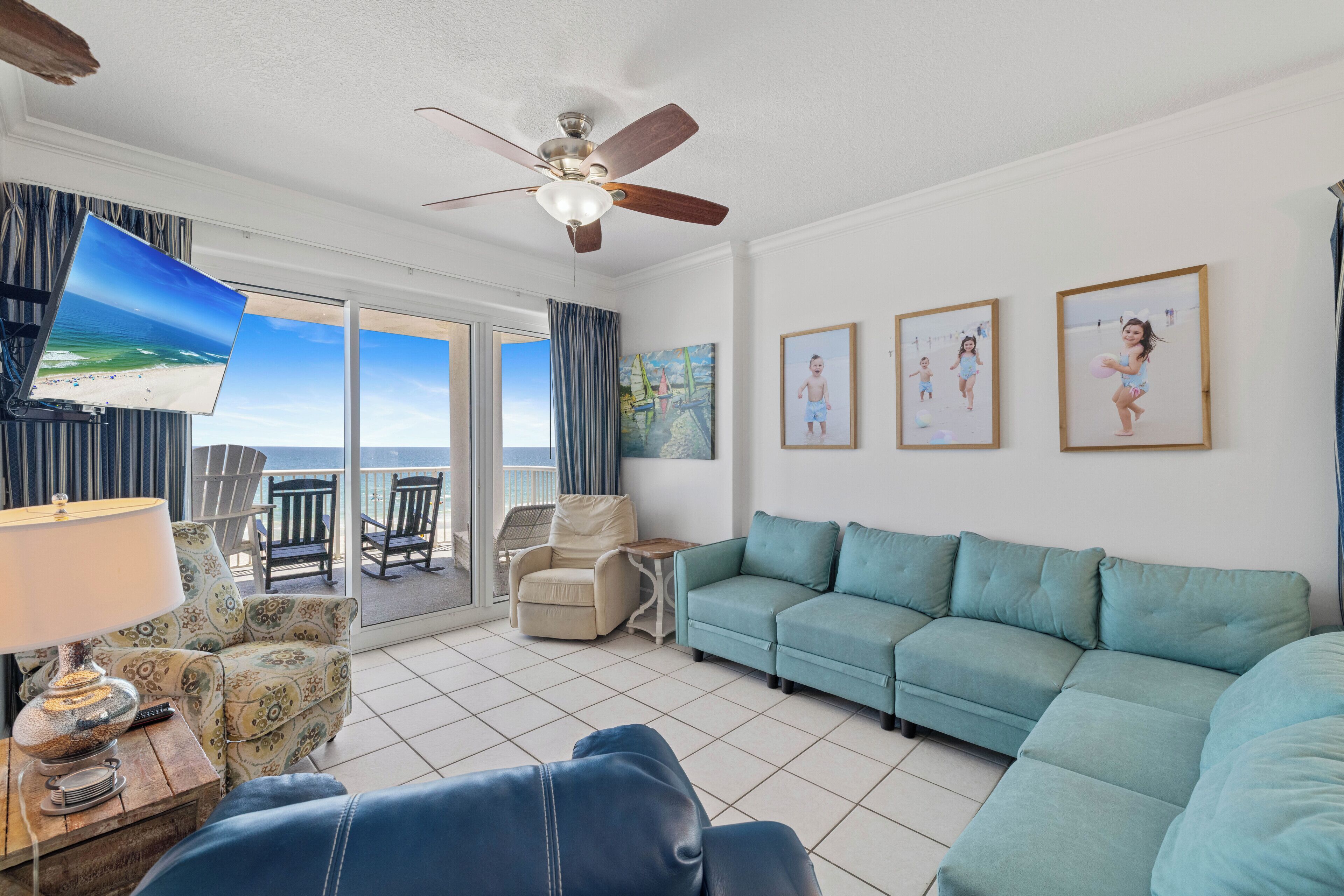 Un salon avec un canapé de couleur turquoise, un ventilateur de plafond, un téléviseur et une vue sur la plage.