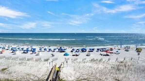 Une plage de sable blanc, avec des parasols bleus et un ciel dégagé.