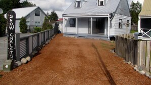 En enkel, lantlig byggnad med en veranda, en grusuppfart och ett trästaket.