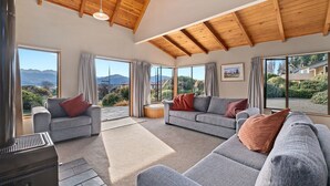 Un salon spacieux avec des canapés gris, une cheminée et de grandes fenêtres offrant une vue sur les montagnes.