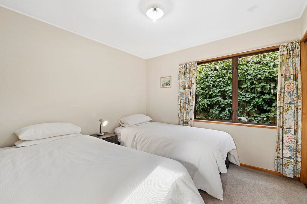 Quarto com duas camas, mesa de cabeceira, janela com cortinas e luz no teto.