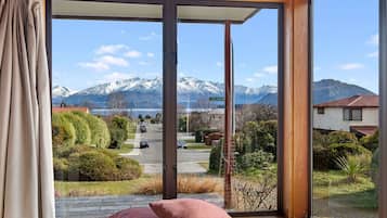 A room with a large window offering a view of a street, snow-capped mountains, and a sign reading "SYCAMOR".