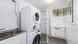 Een moderne badkamer met een ingebouwde wasmachine en droger, een glazen douchecabine en een wastafelmeubel met een wastafel en spiegel.