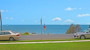 A coastal road with a 'NO ENTRY' sign, a 'FLYNNS BEACH' sign, and two parked cars.