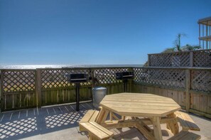 A wooden deck with a picnic table and grill, overlooking a body of water.