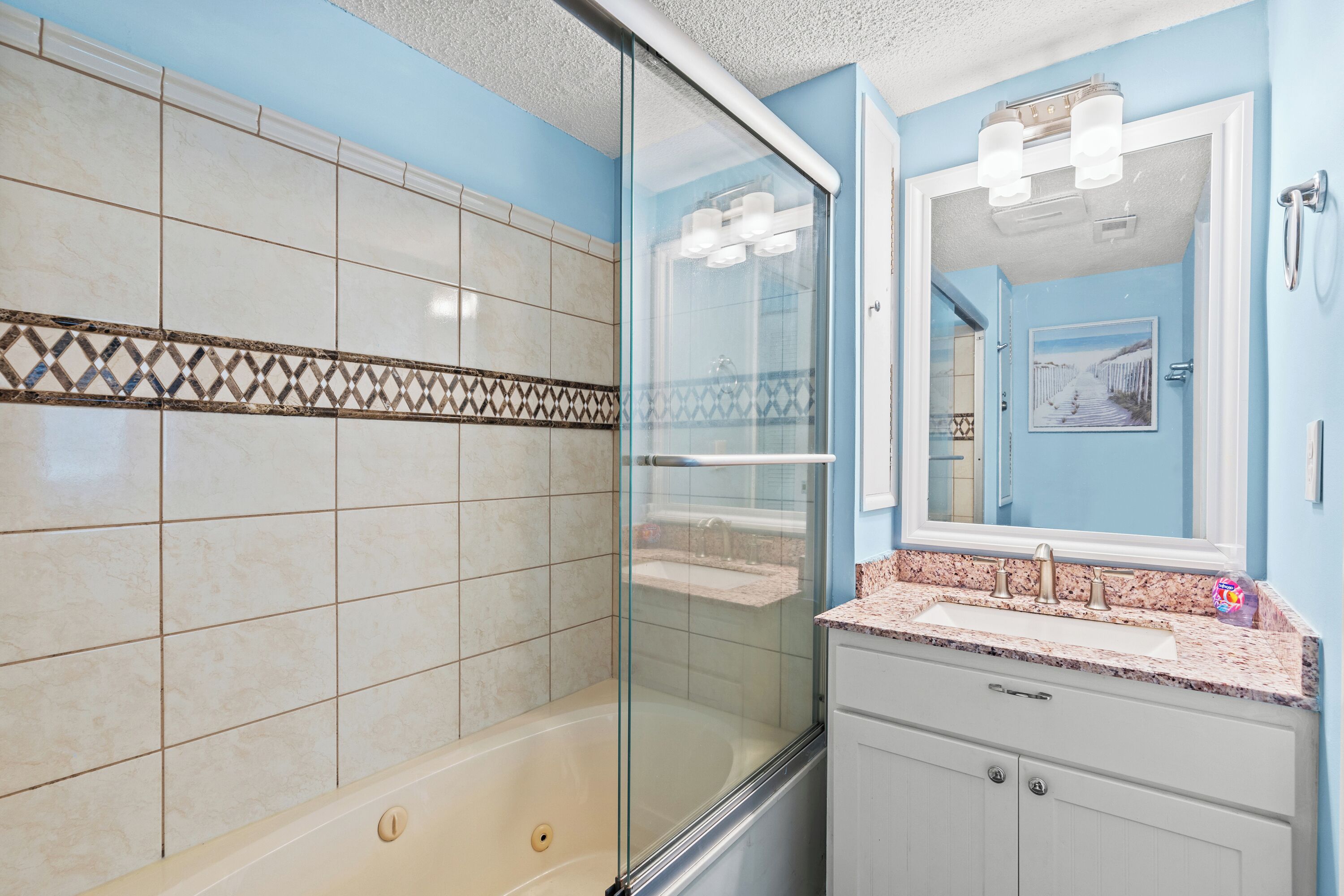 A bathroom with a glass-enclosed shower, a sink with a marble countertop, and a mirror above the sink.