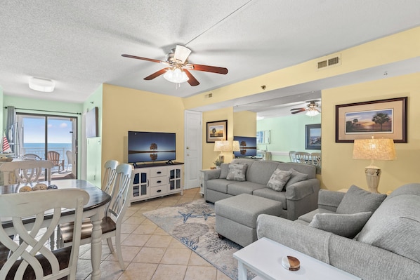 A living room with a sofa, armchairs, a dining table with chairs, a ceiling fan, and a television.