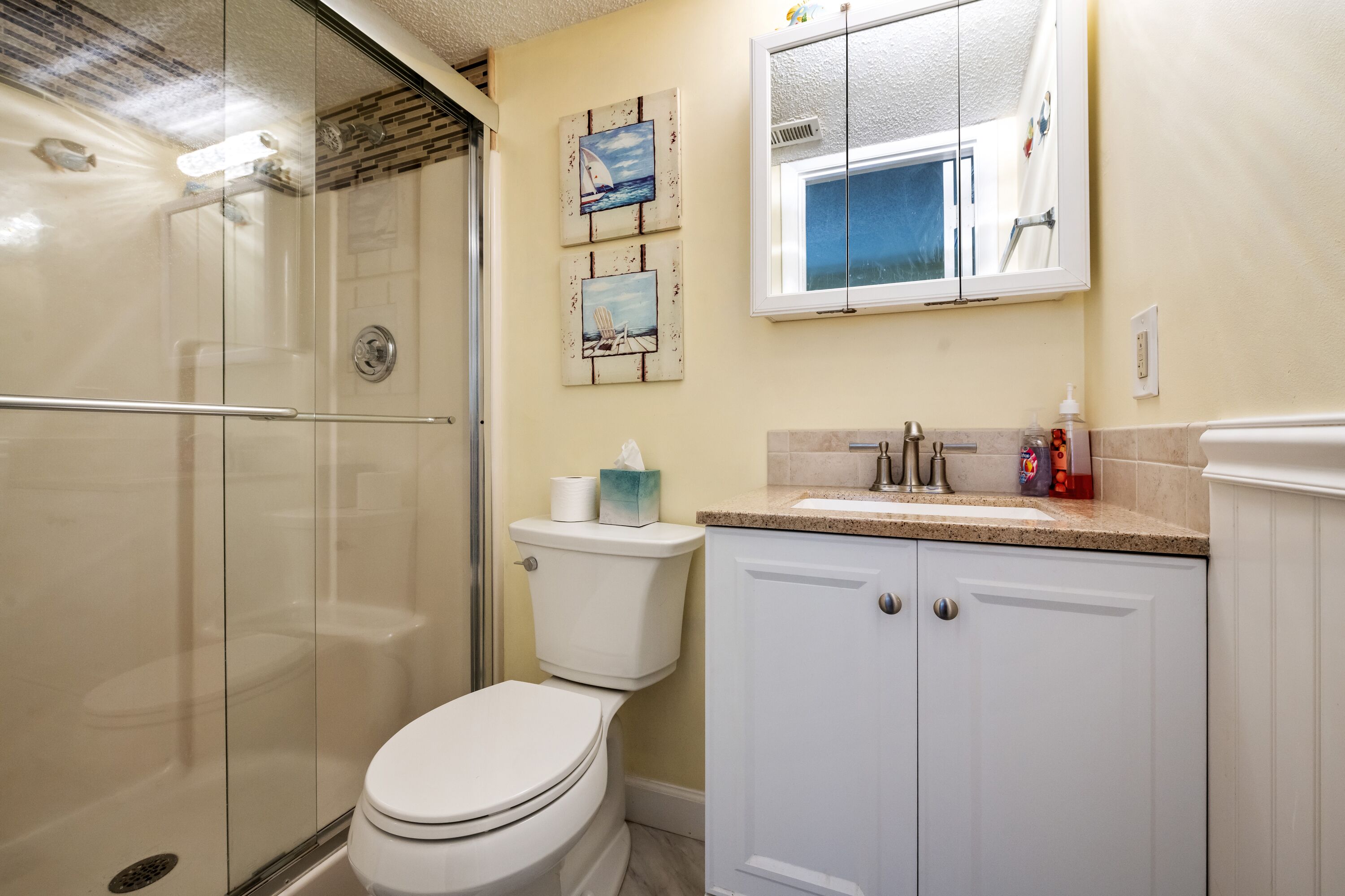 A bathroom with a glass-enclosed shower, a toilet, and a sink with a mirror above.