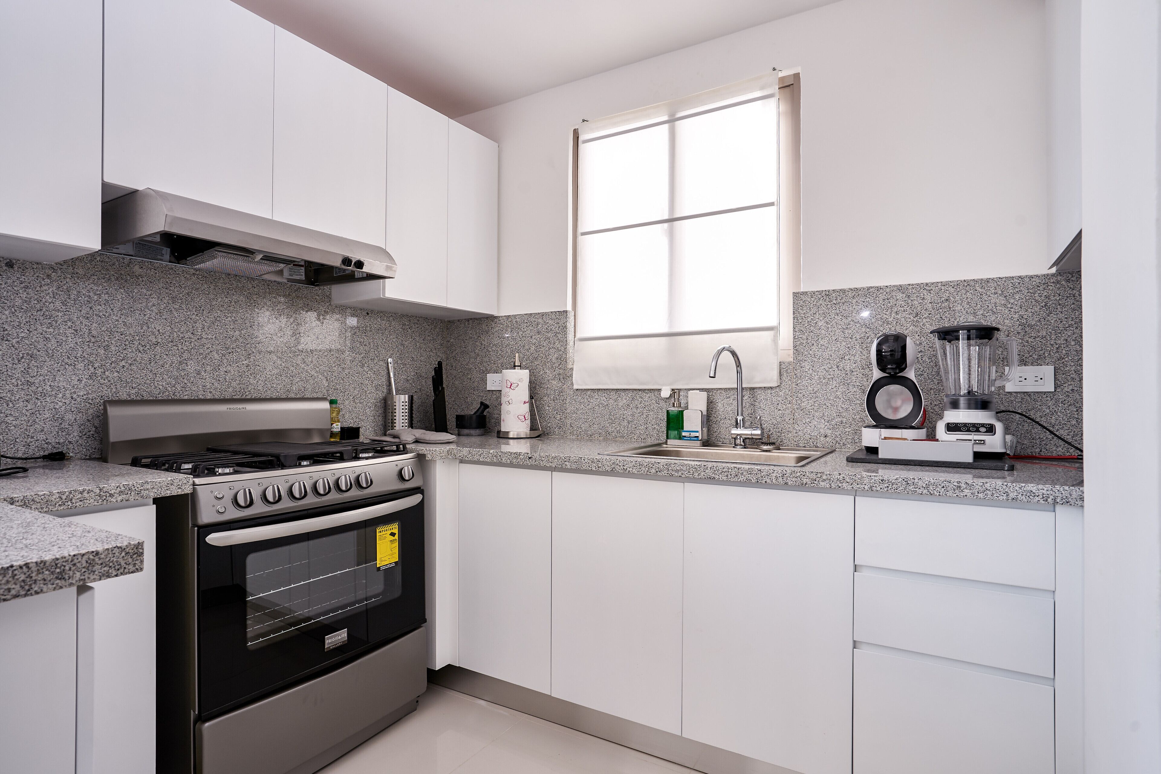Una cucina moderna con piano cottura a gas, forno, ripiano in granito e una finestra che lascia entrare luce naturale.