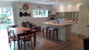 A modern kitchen with a central island, dining area with wooden table and chairs, and a view of greenery outside.