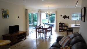 A living room with a television, a sofa, a dining table with chairs, and a kitchen area with a sink and a fish decoration.