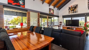 A modern living room with a wooden dining table, grey sofas, and a large flat-screen TV.