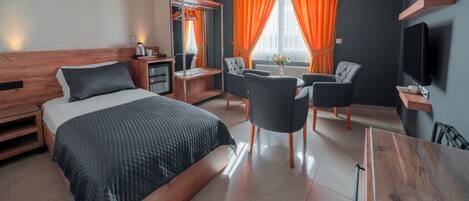 A hotel room with a bed, a desk, a chair, a TV, and a window with curtains.